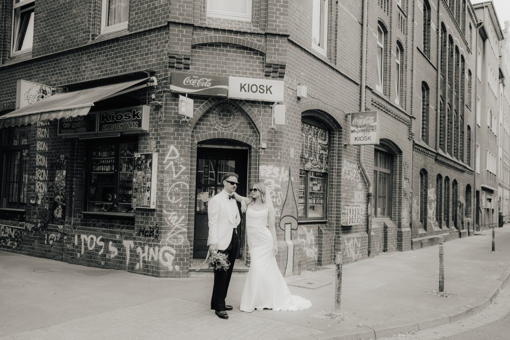 Brautpaar steht lässig im Brautpaatshooting vor einem Kiosk.